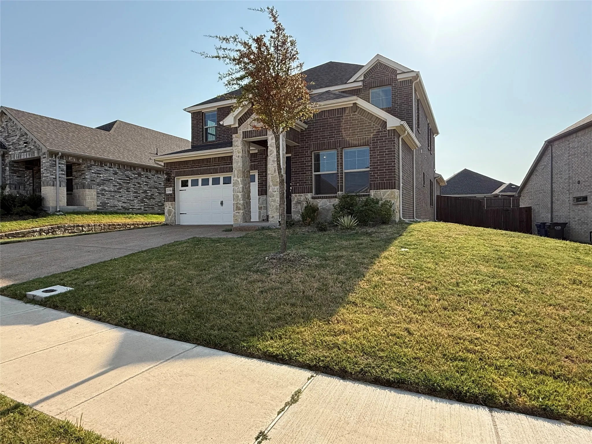Brick and stone veneer exterior with a two-car garage, concrete driveway, and established front yard landscaping