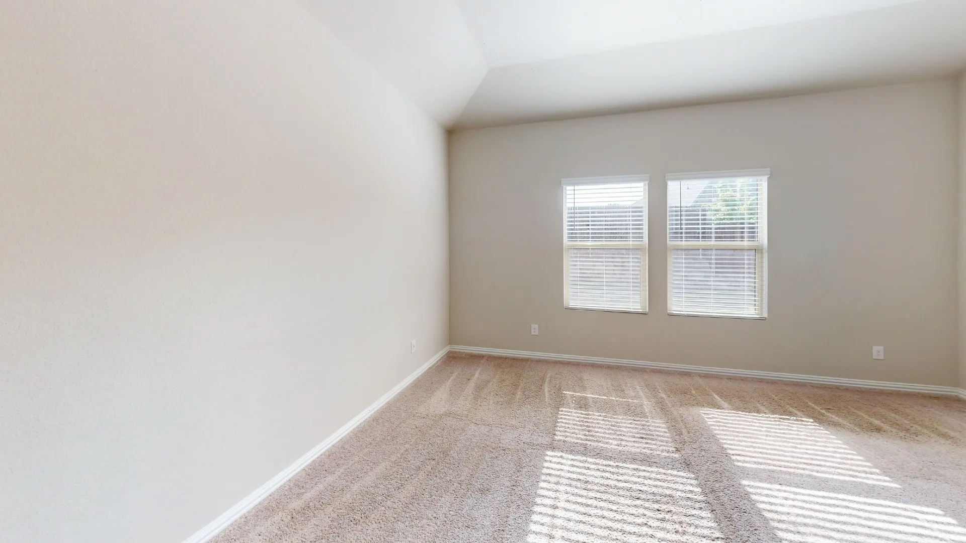 Vaulted ceiling, neutral wall paint, two windows with horizontal blinds, and carpeted flooring
