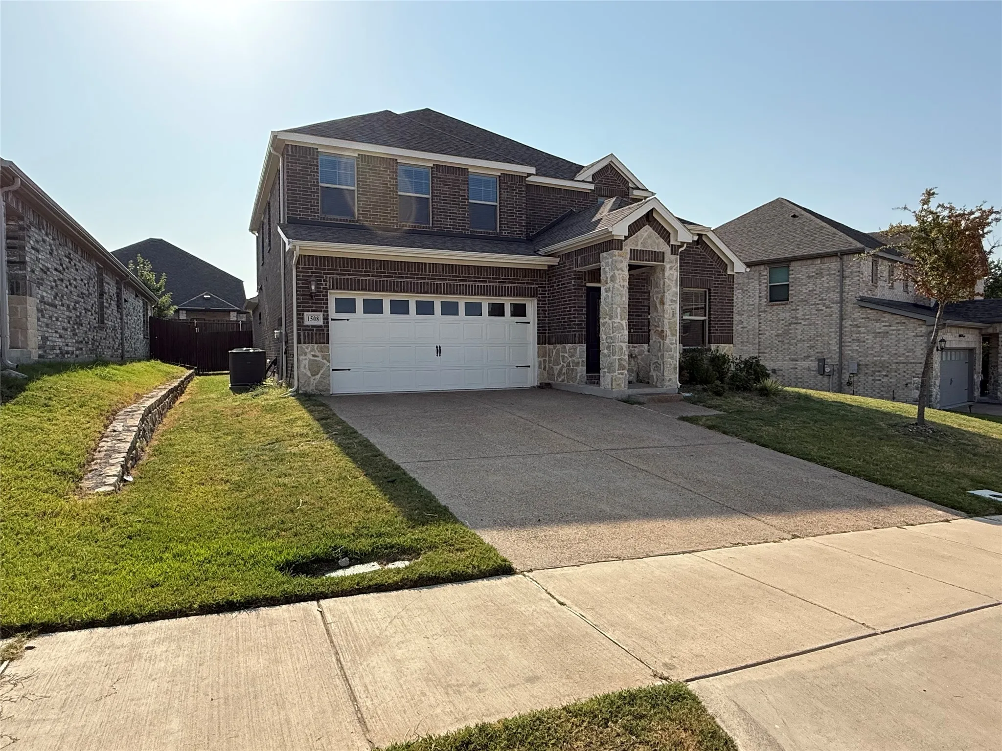 Brick and stone exterior with a two-car garage, concrete driveway, and front lawn
