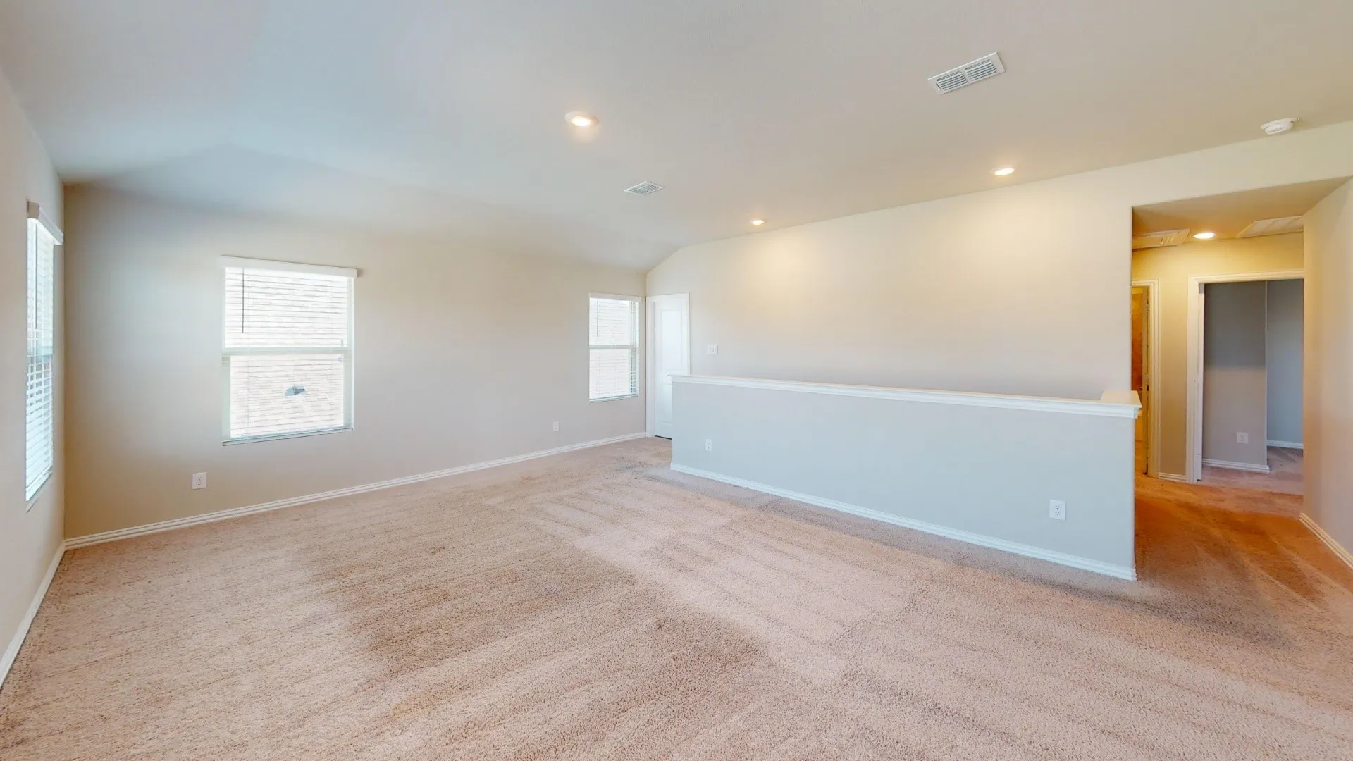 Spacious room featuring carpet flooring, recessed lighting, multiple windows with blinds, and a partial wall