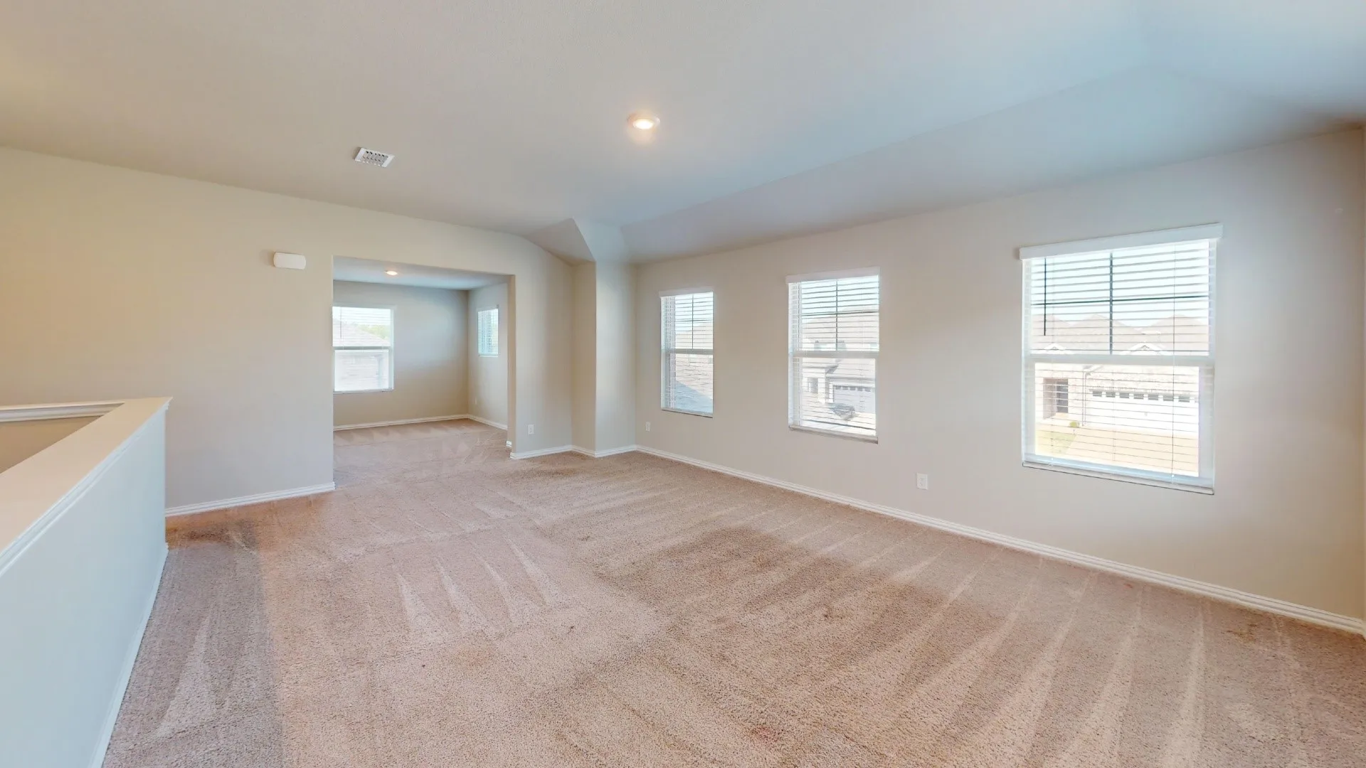 Expansive carpeted area featuring light neutral wall tones, multiple windows with blinds, and recessed lighting