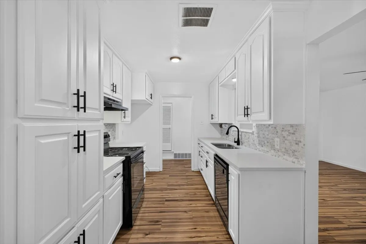 White shaker cabinetry with matte black hardware, stone countertops, mosaic tile backsplash, black kitchen appliances, and wood-finish flooring
