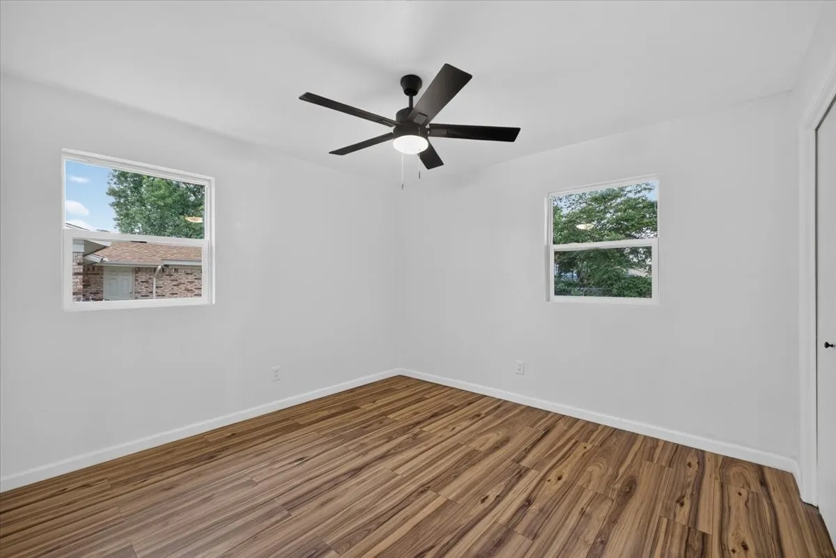 Wood-finish flooring, white walls, two windows, and a ceiling fan with integrated lighting