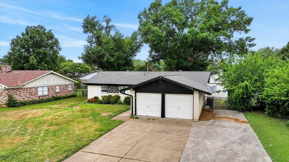 Two-car garage with white doors, concrete driveway, and mature landscaping