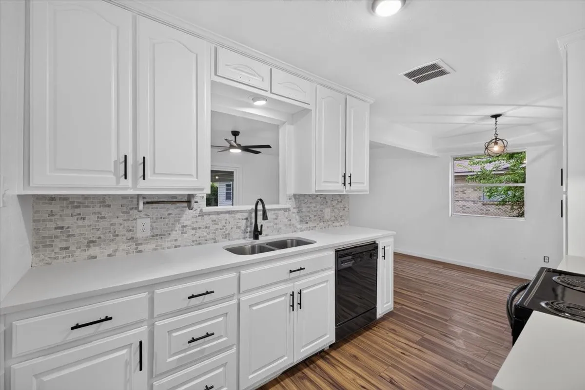 White cabinetry with black hardware, mosaic tile backsplash, double basin sink with a black gooseneck faucet, black dishwasher, and wood-finish flooring