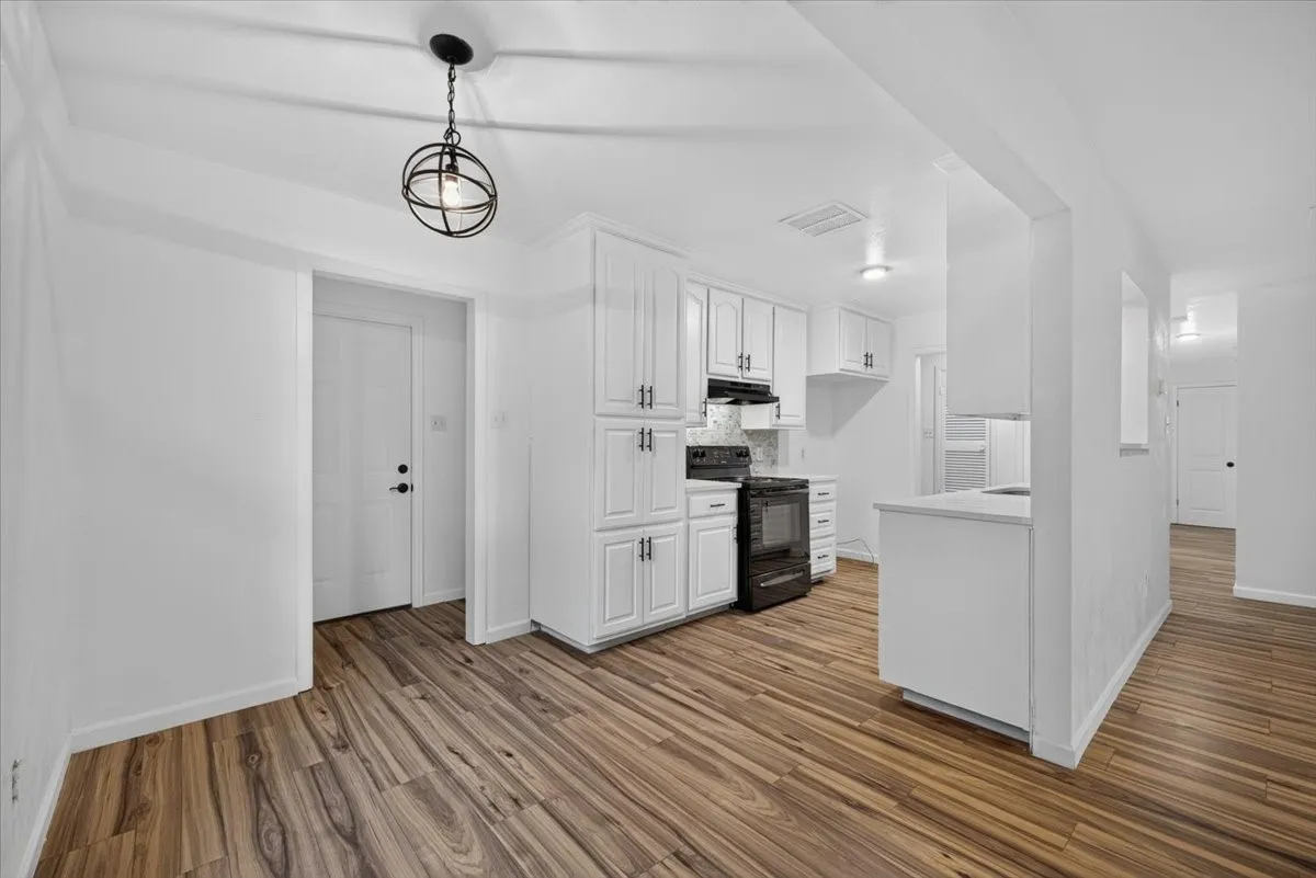 Kitchen featuring white cabinetry, wood-finish flooring, a black electric range, and a breakfast bar