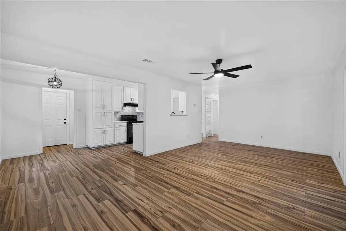 Wood-finish flooring, white walls, white cabinetry, integrated black range with hood, and a ceiling fan