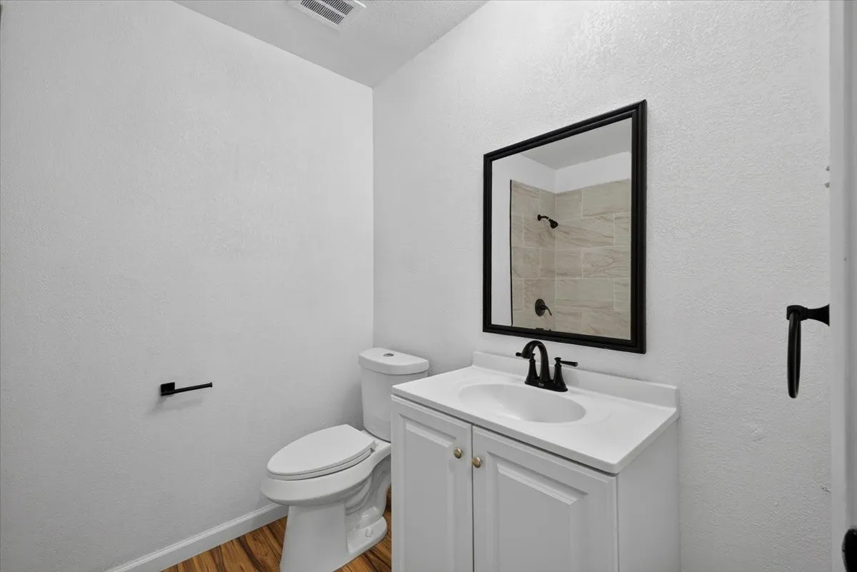 White vanity with integrated sink and matte black faucet, framed mirror, and wood-finish flooring