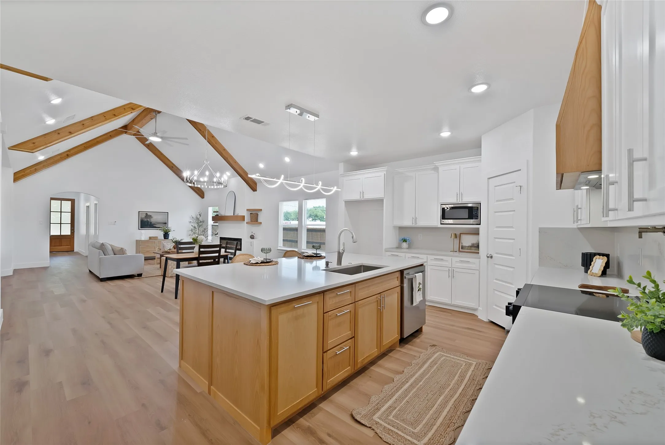 Kitchen with wood-finish flooring, light wood-tone island cabinetry, white perimeter cabinetry, stainless steel appliances, and light-toned countertops