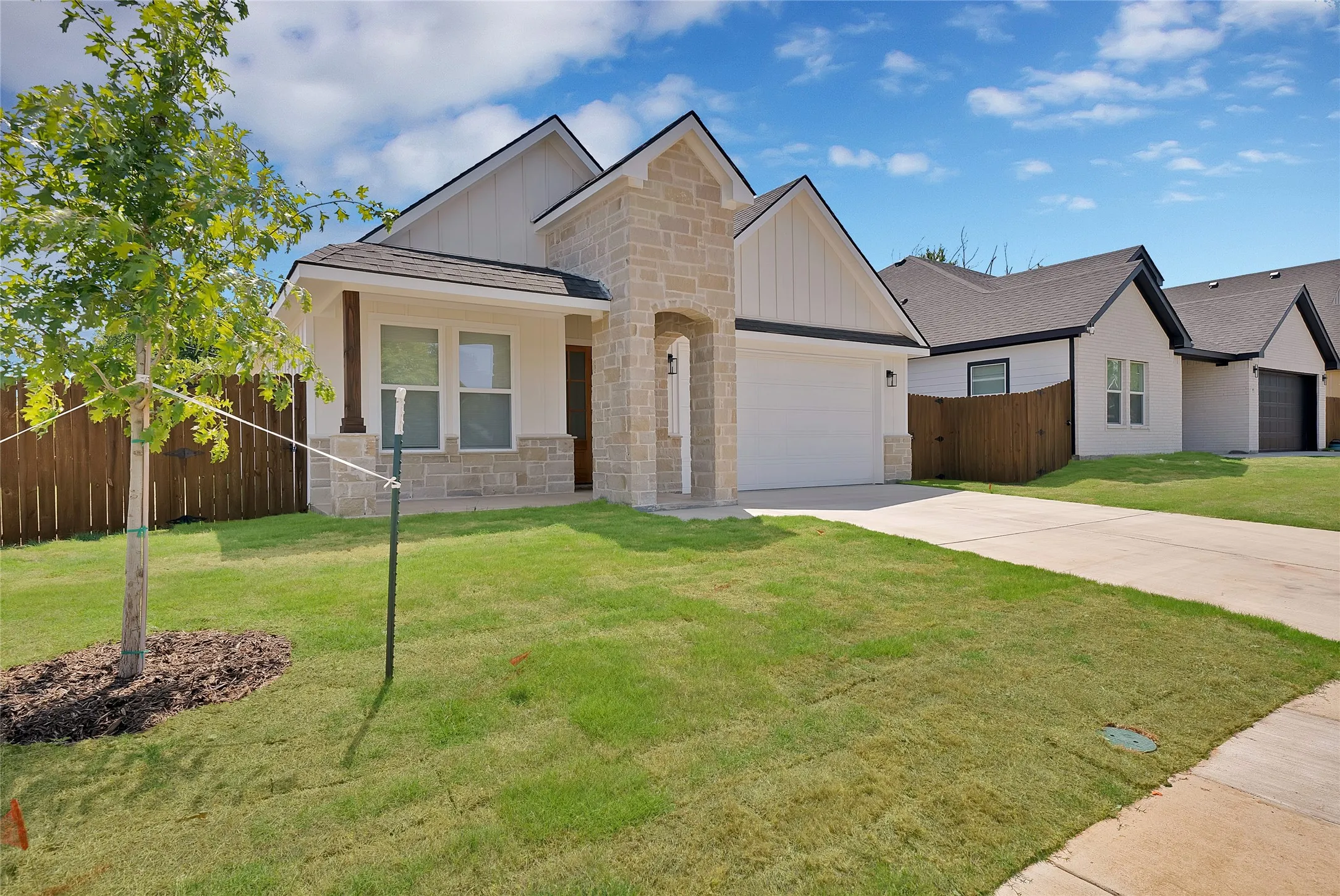 Gabled roofline, stone and siding exterior, front-facing garage, concrete driveway, and a wood privacy fence
