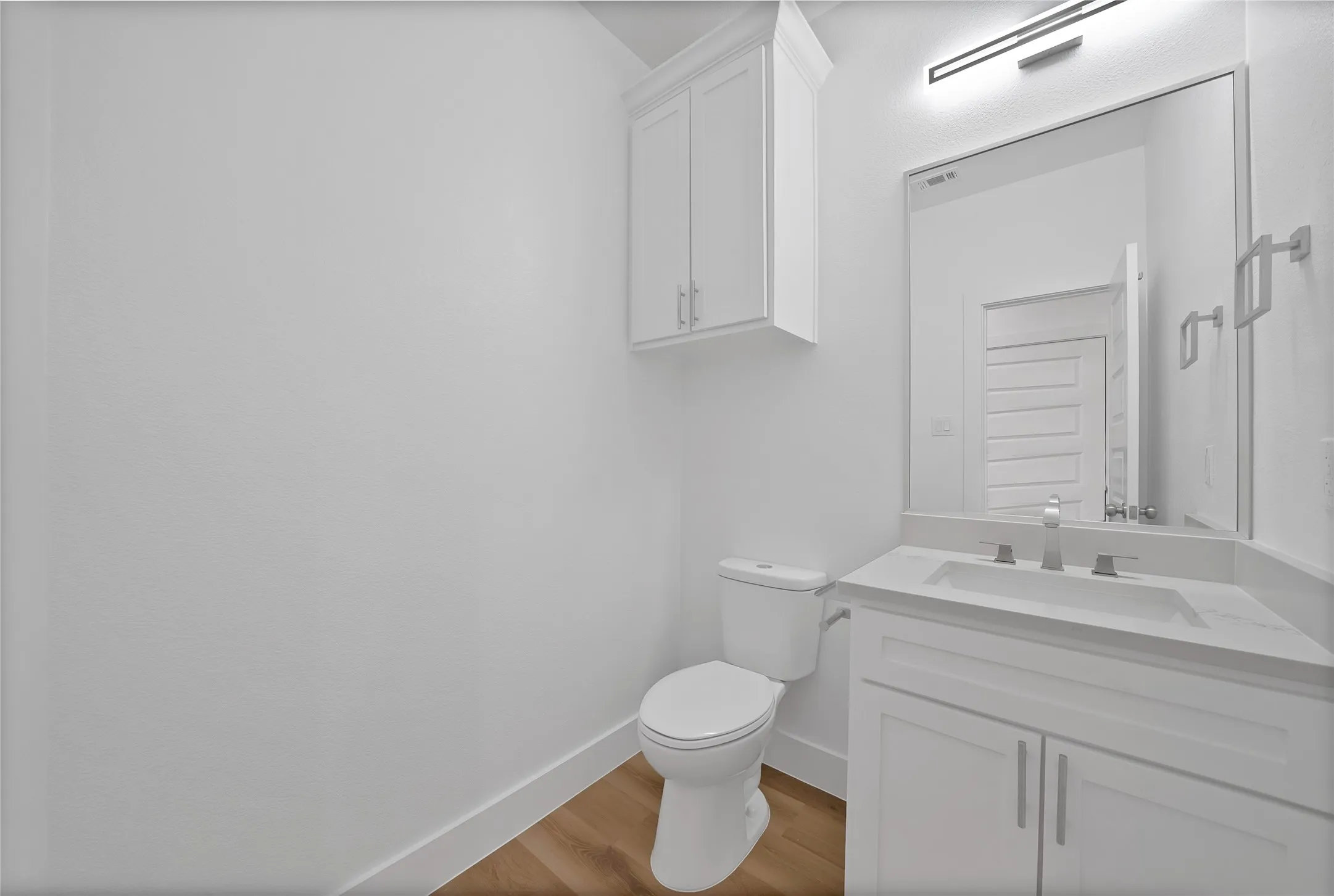 White cabinetry with upper storage, recessed sink, light-toned countertop, and wood-finish flooring