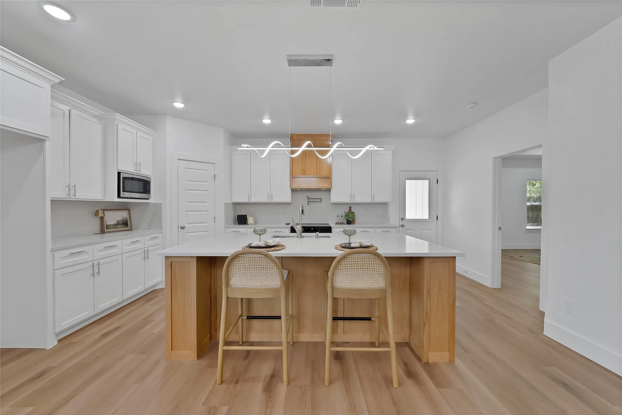 Open-concept kitchen with white shaker cabinetry, an island with wood-finish paneling, light wood-finish flooring, and white countertops