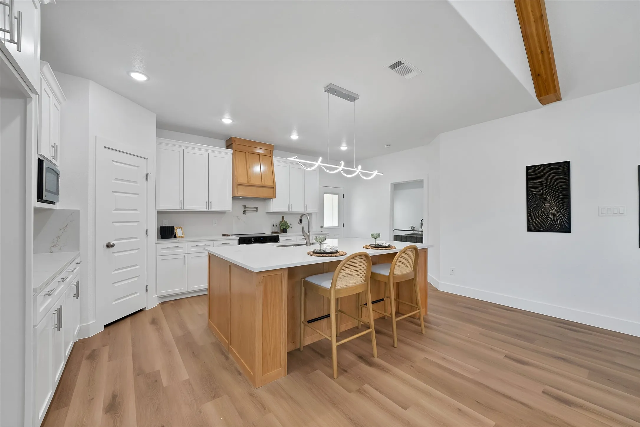 Open-concept kitchen with a light wood-finish island, white cabinetry, integrated appliances, and wood-finish flooring