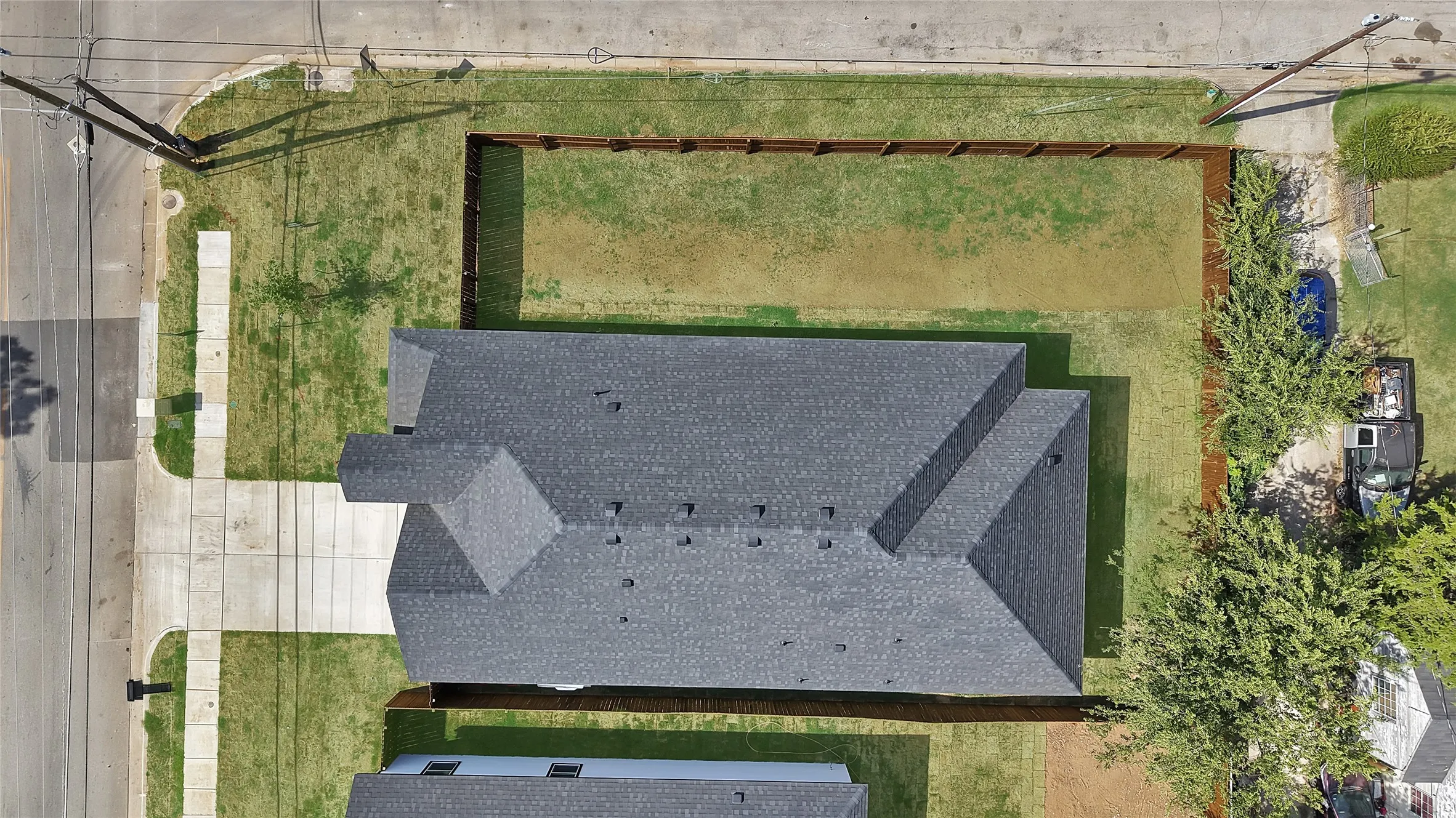 Gable roof design with dark grey shingles, expansive concrete driveway, and a partially fenced yard