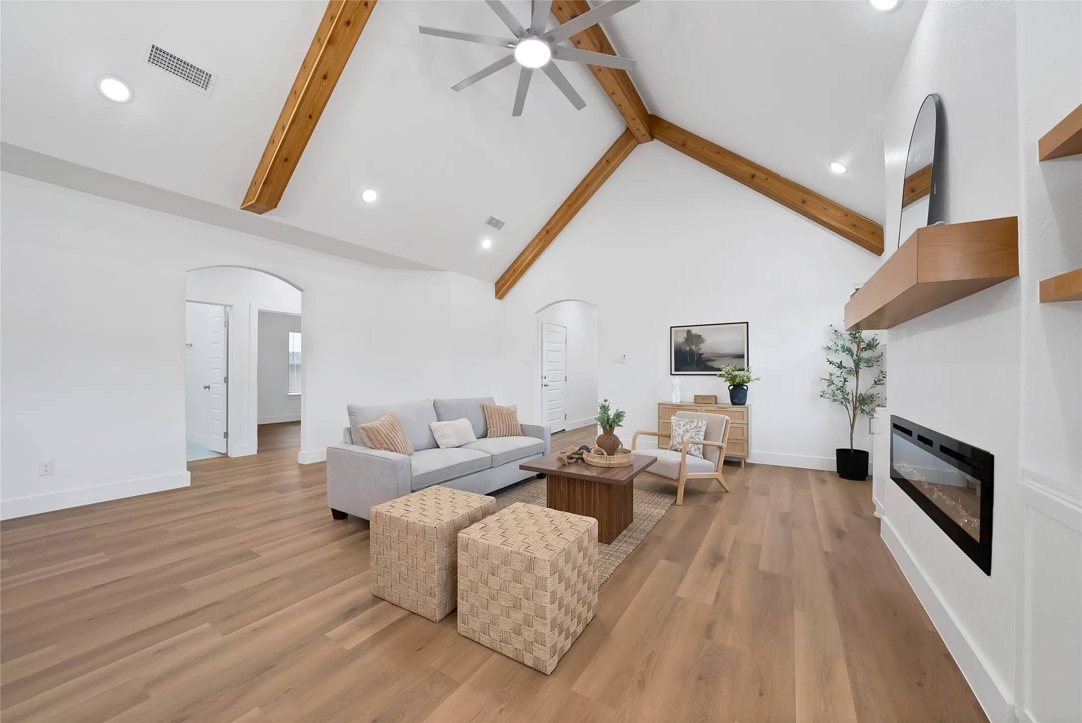 Vaulted ceiling with exposed wood beams, wood-finish flooring, built-in electric fireplace, recessed lighting, and a ceiling fan