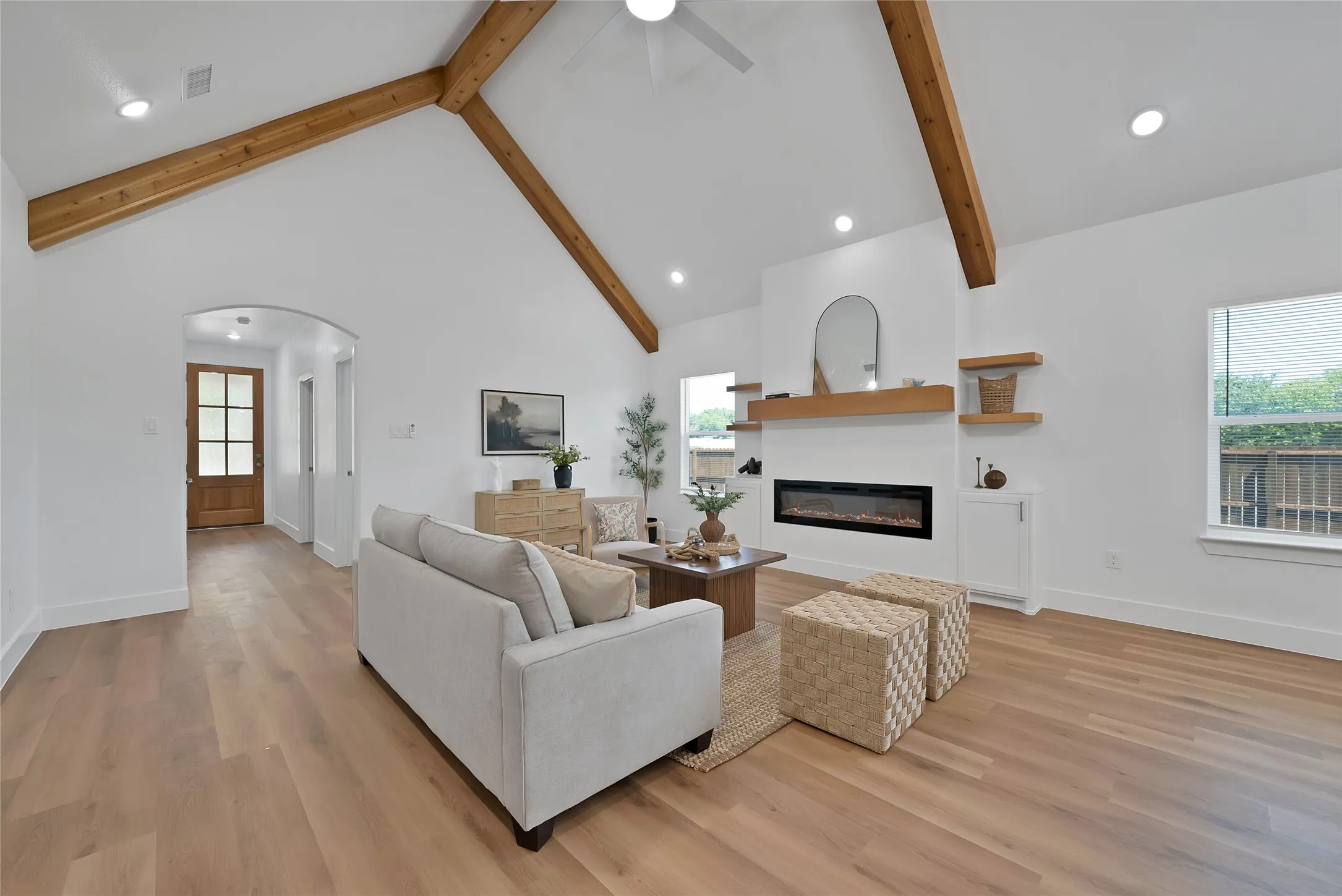 Vaulted ceiling with exposed wood beams, recessed lighting, wood-finish flooring, built-in electric fireplace, and an arched entry