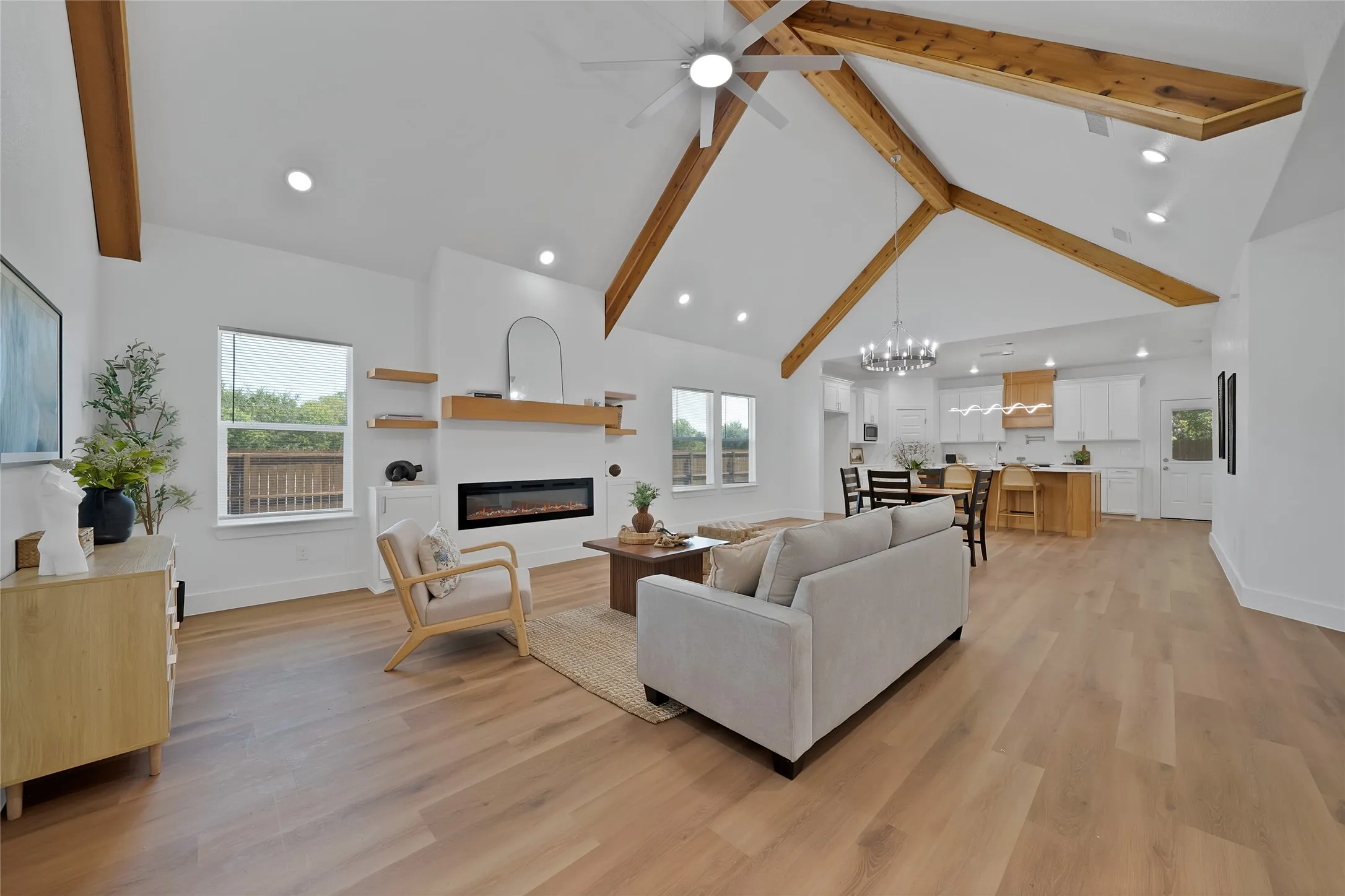 Vaulted ceiling with exposed wood beams, wood-finish flooring, recessed lighting, built-in electric fireplace, and a ceiling fan