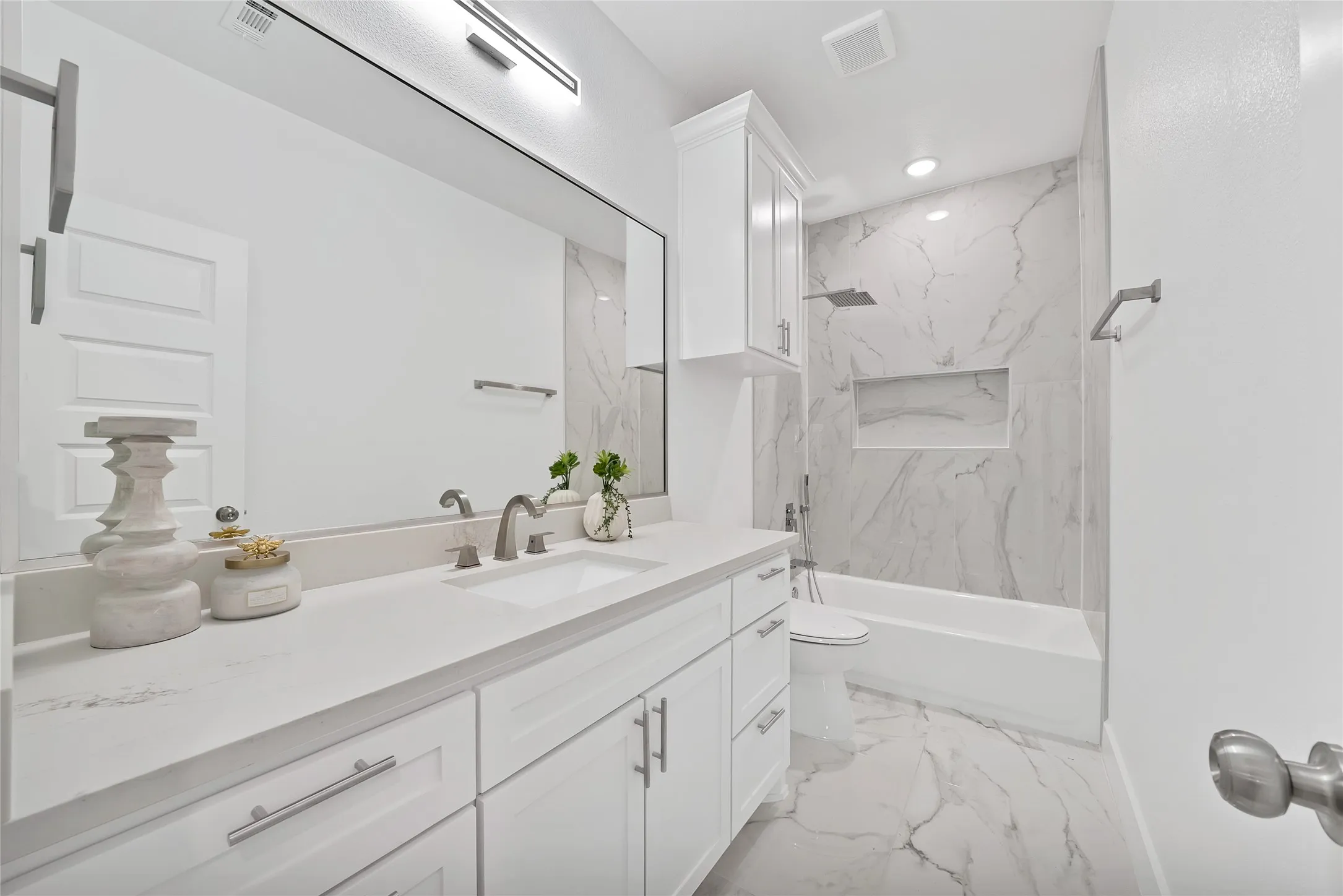 White vanity with dual sinks, a large mirror, and a sleek linear light fixture