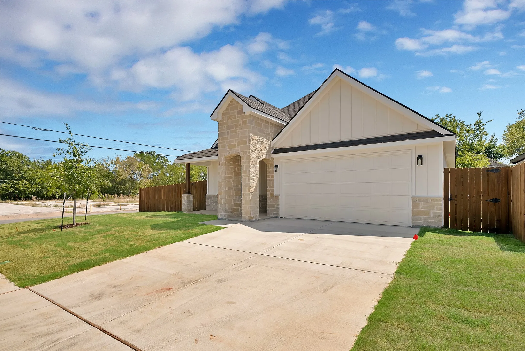 Stone and vertical siding exterior with a two-car garage, concrete driveway, and established lawn