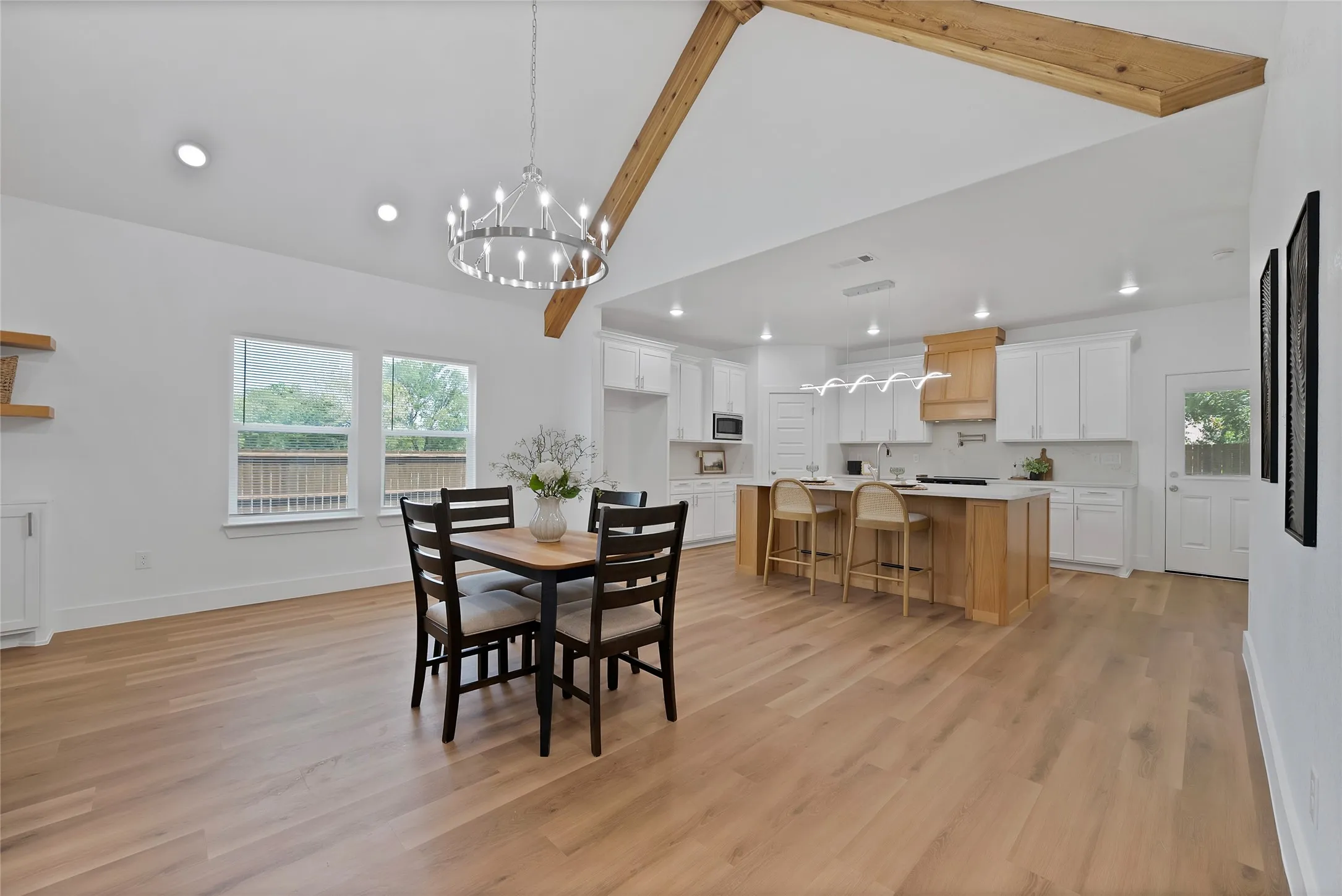 Vaulted ceiling with exposed wood beams, wood-finish flooring, recessed lighting, and a kitchen featuring white cabinetry, a central island, and a wood-finish range hood