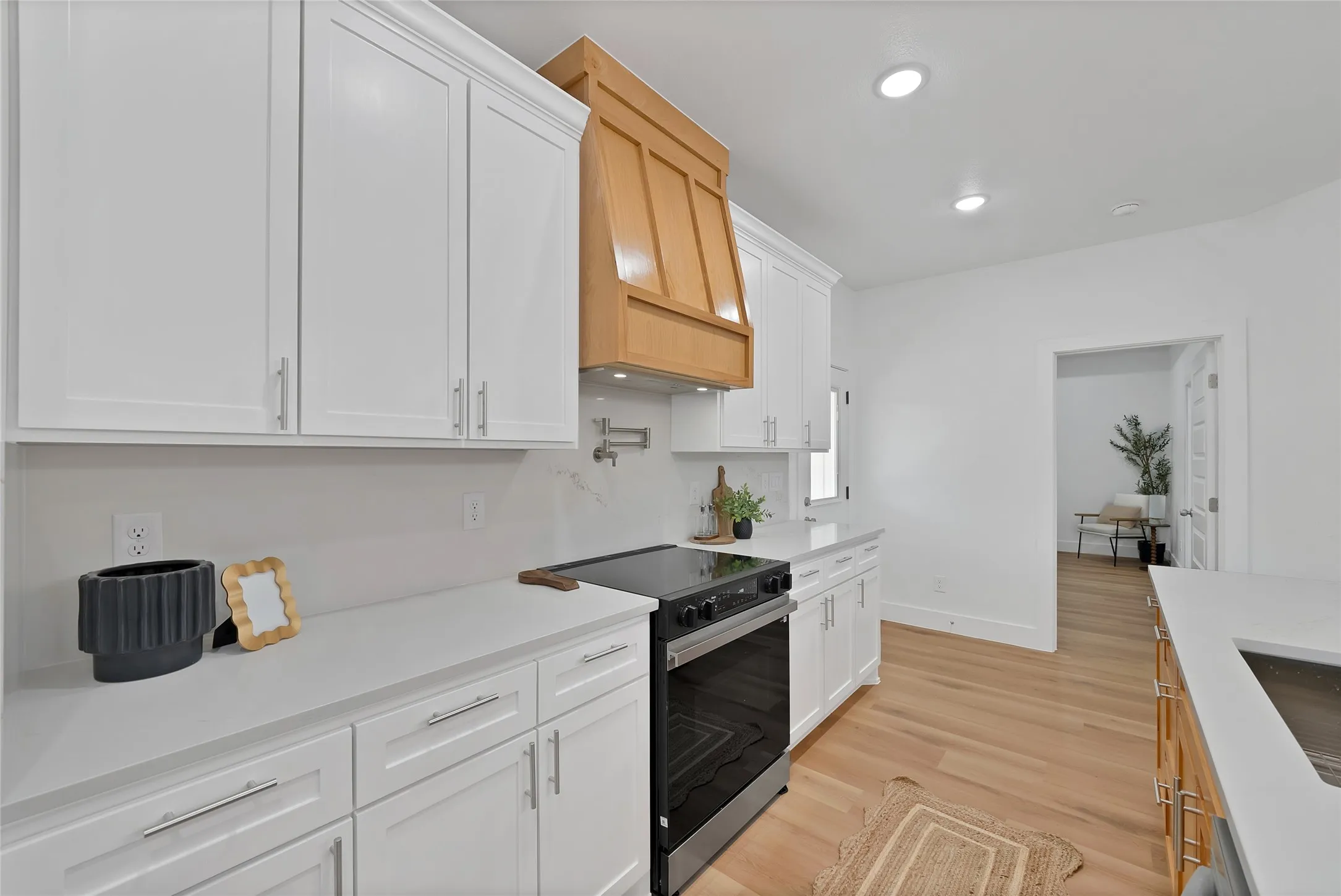 White cabinetry, wood-finish flooring, recessed lighting, and a wood-finish range hood