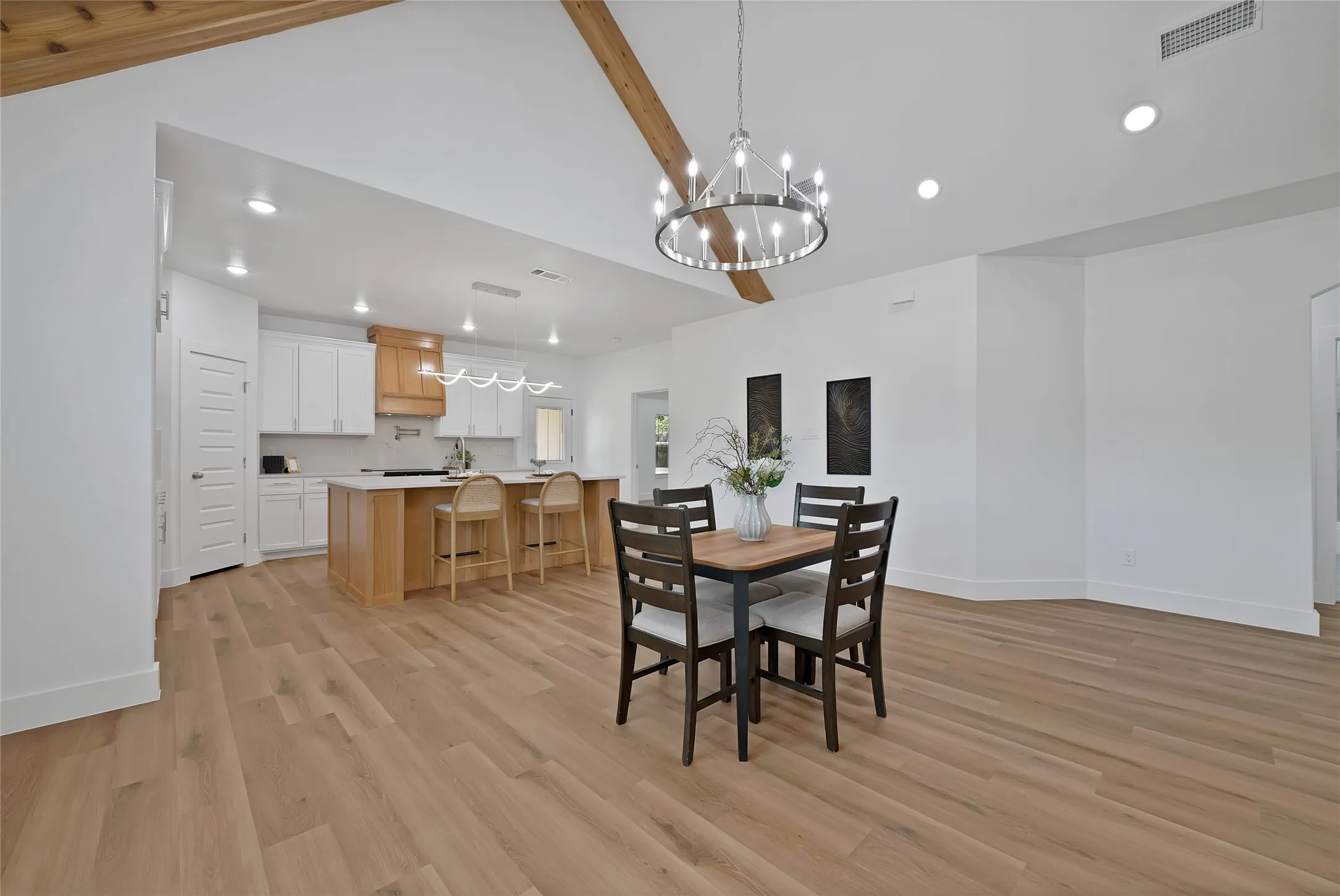 Vaulted ceiling with exposed wood beams, wood-finish flooring, recessed lighting, white perimeter cabinetry, and a central kitchen island