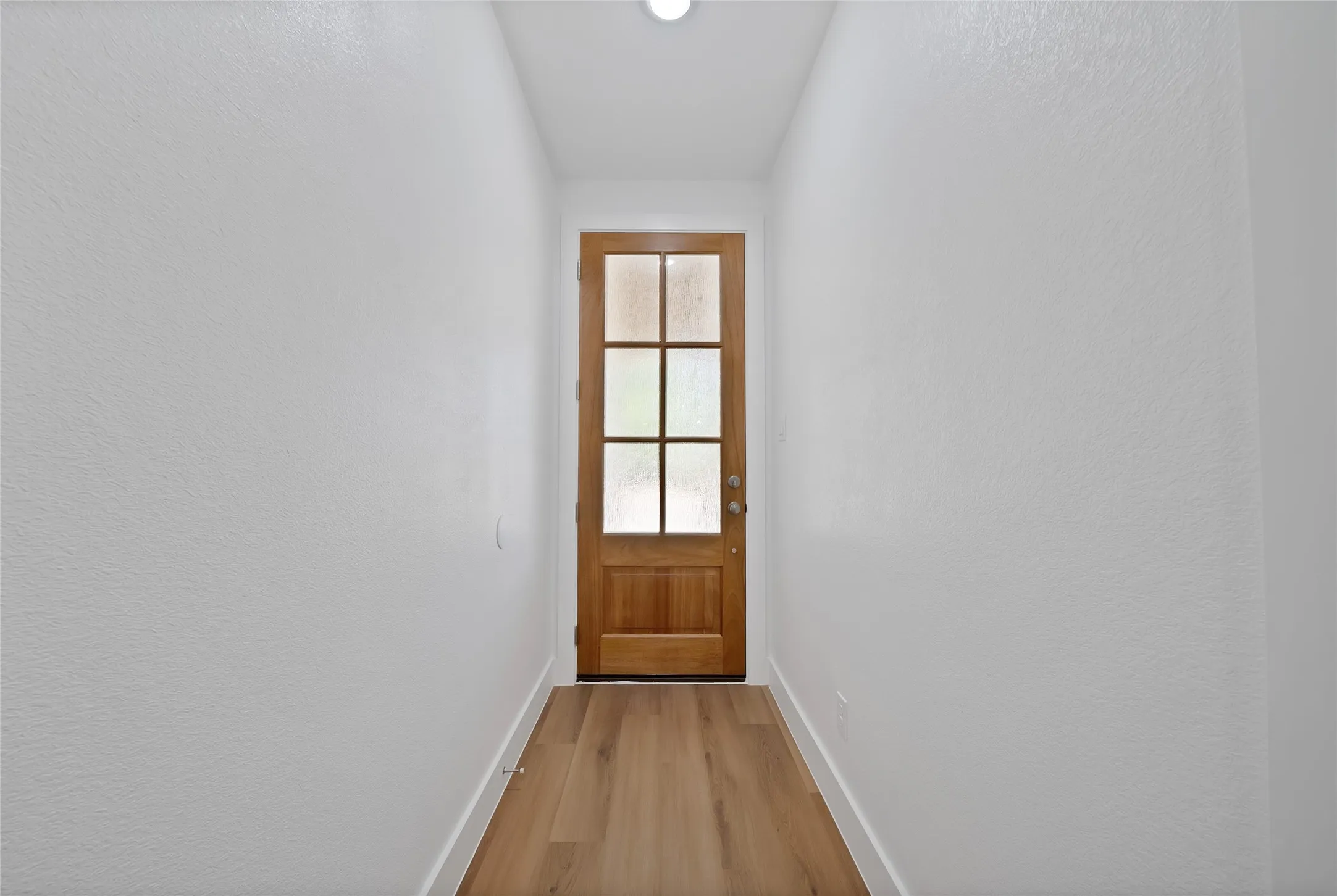 Wood-finish flooring leading to a wooden door with frosted glass panels