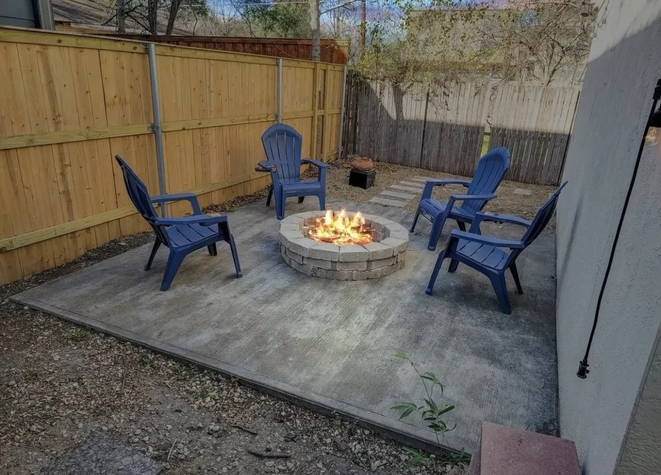 Concrete patio with a stone fire pit, wood privacy fencing, and a gravel area