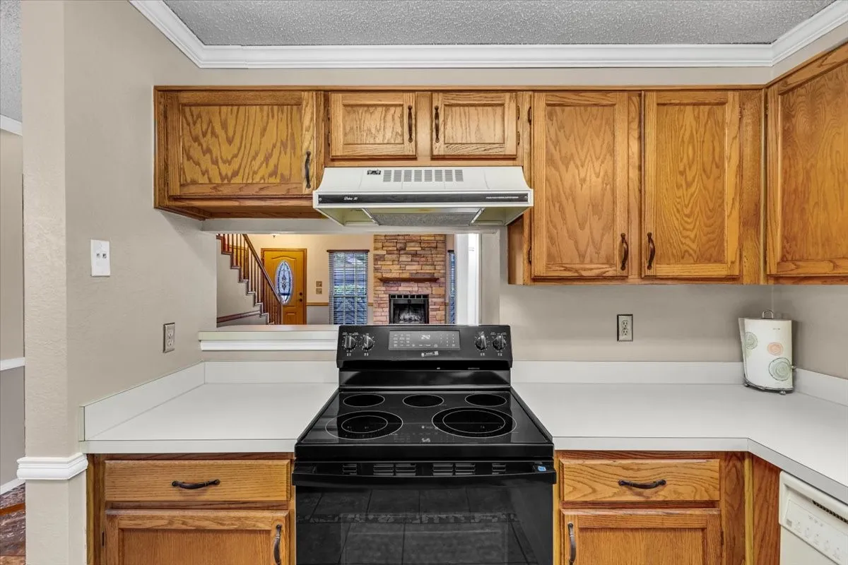 Kitchen featuring wood cabinetry, white countertops, black new electric range, and a built-in range hood