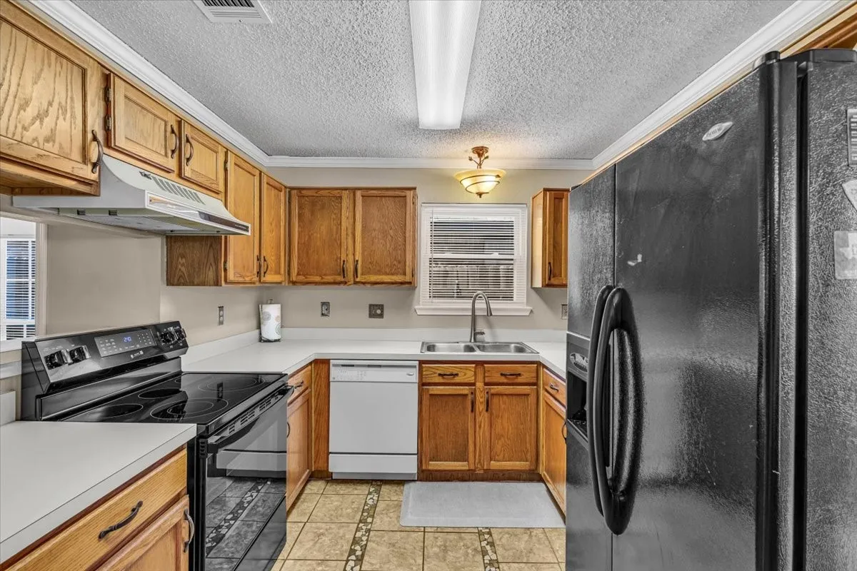 U-shaped kitchen with wood cabinetry, white countertops, tile flooring, and integrated appliances. The refrigerator is negoiatable.