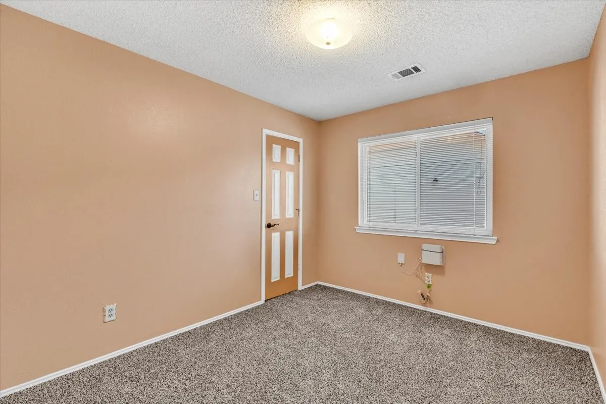 Window with blinds, wood-paneled door, textured ceiling, wall-mounted light fixture, and carpeted flooring.
