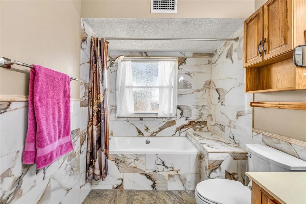 Bathtub with surrounding tile, wood-finish cabinetry, and tiled flooring