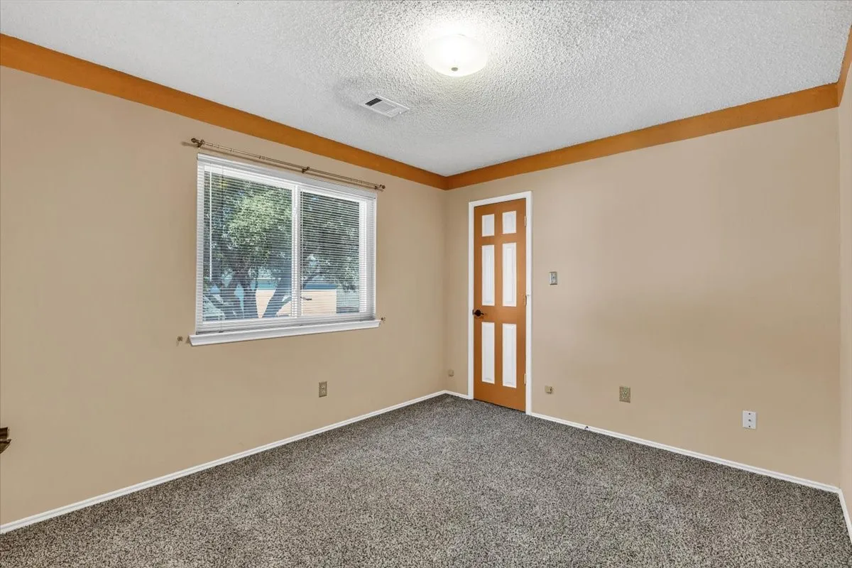 Window with blinds, wood-paneled door, textured ceiling, wall-mounted light fixture, and carpeted flooring