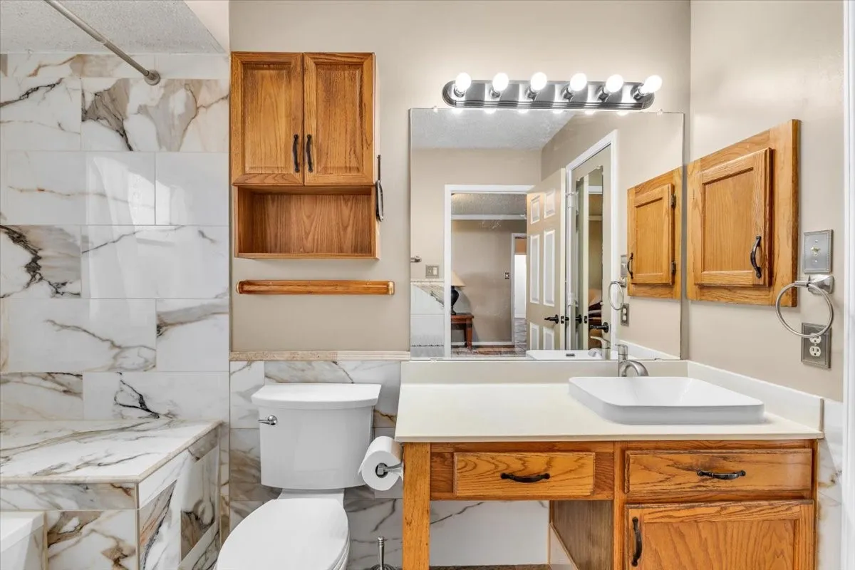Porcelain tile shower surround with integrated bench, a wood-finish vanity with countertop basin, and upper wood-finish storage cabinetry