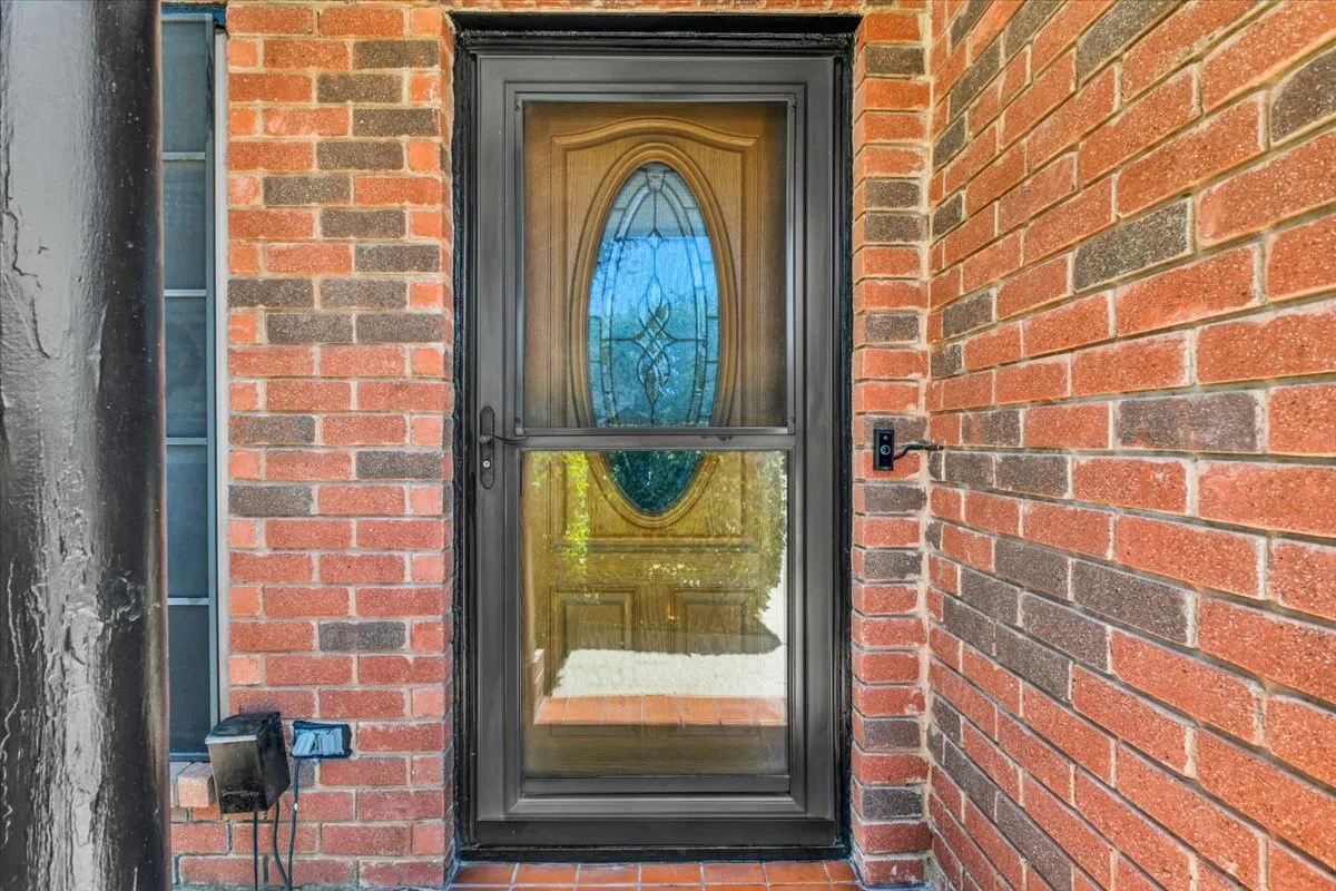Brick exterior featuring a black storm door, wood-finish entry door with an oval glass insert, and a sidelite window