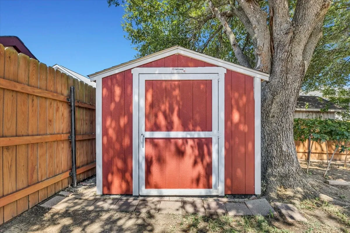 Red-painted Tuff Shed storage shed with white trim, wood privacy fence, and mature tree