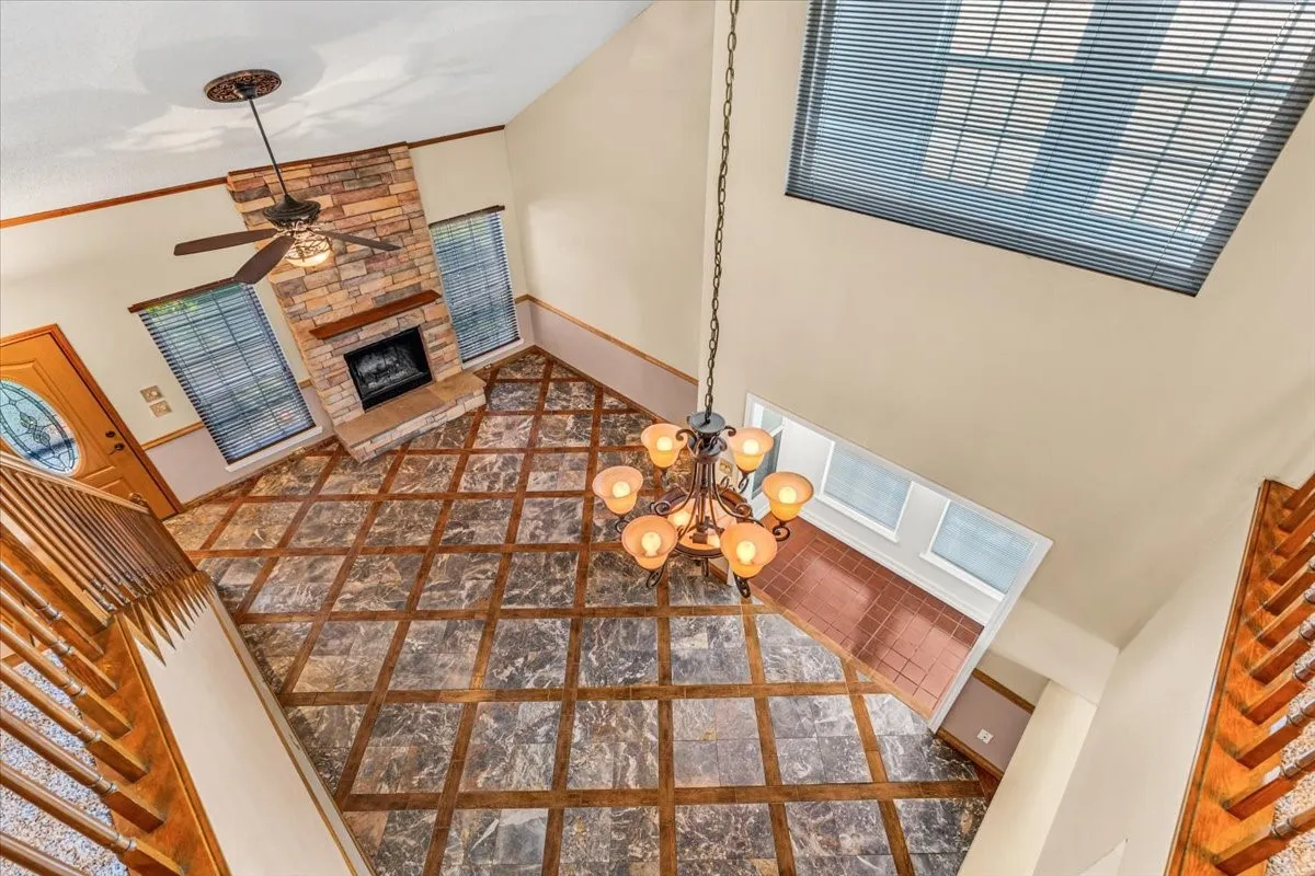 This living room view features soaring ceilings with transom windows, a stone-clad fireplace, and an elegant chandelier.