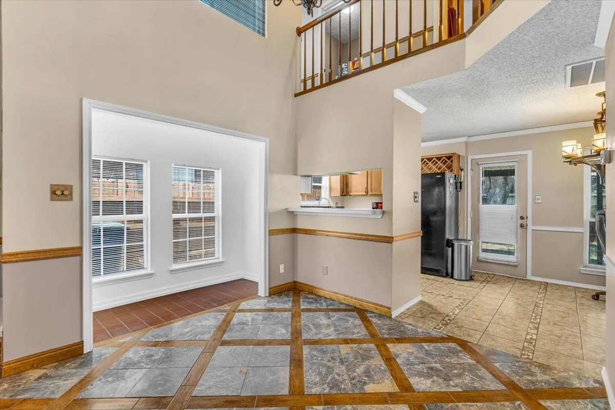 Soaring ceilings with transom windows, stone-clad fireplace, and an elegant chandelier, open to the Dining Room and Kitchen.