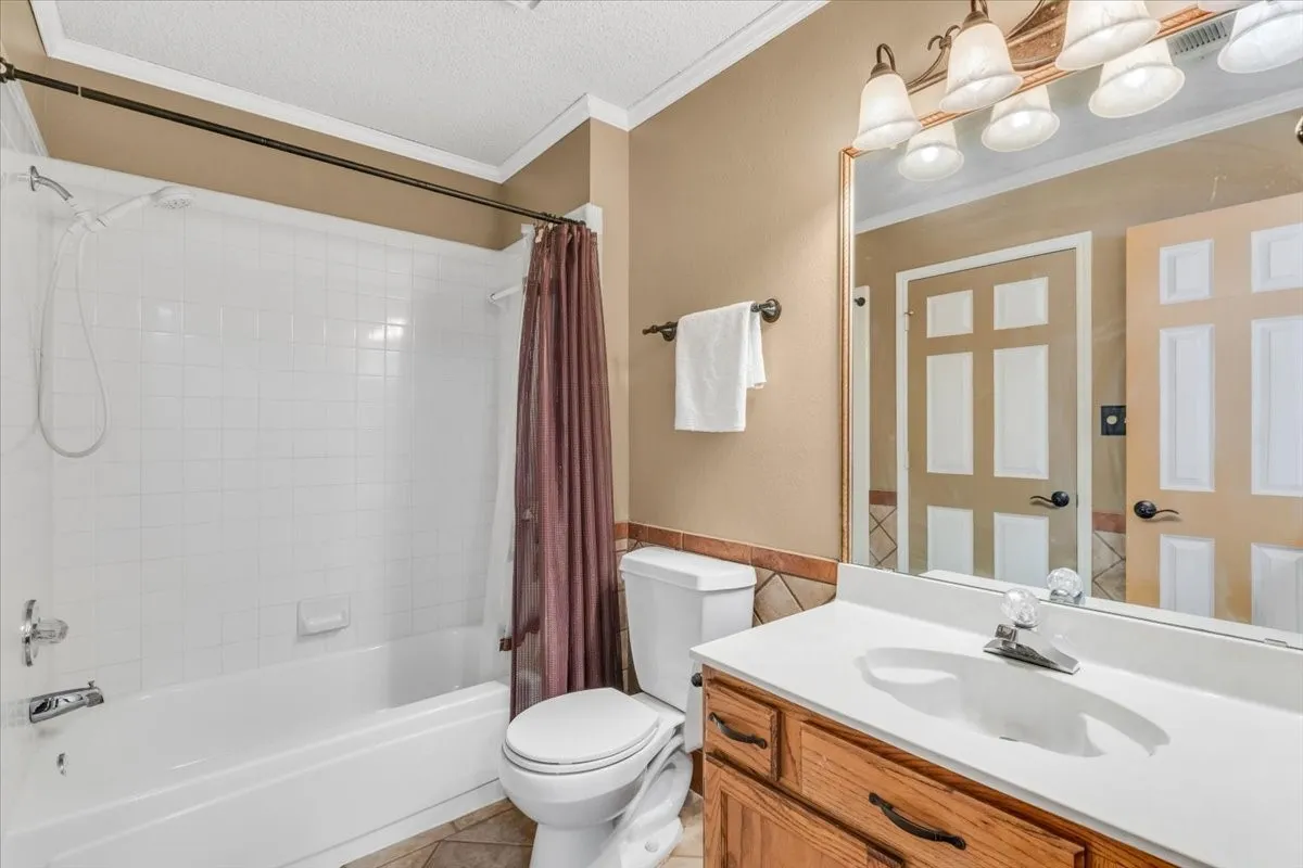 Bathroom featuring a white subway tile shower surround, a built-in bathtub, a wood-finish vanity with a white countertop and integrated sink, and an overhead vanity light fixture.