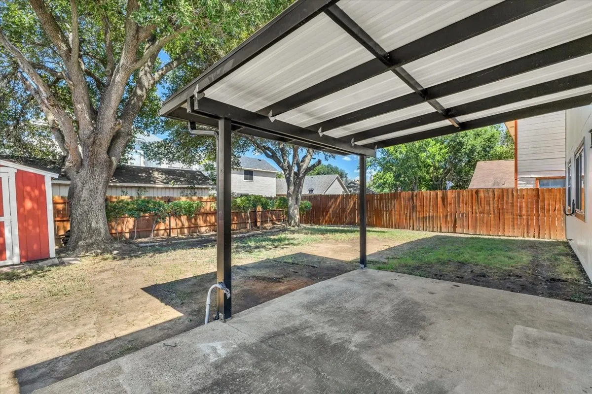 Covered patio with a concrete surface, fenced backyard, mature trees, and an exterior storage shed