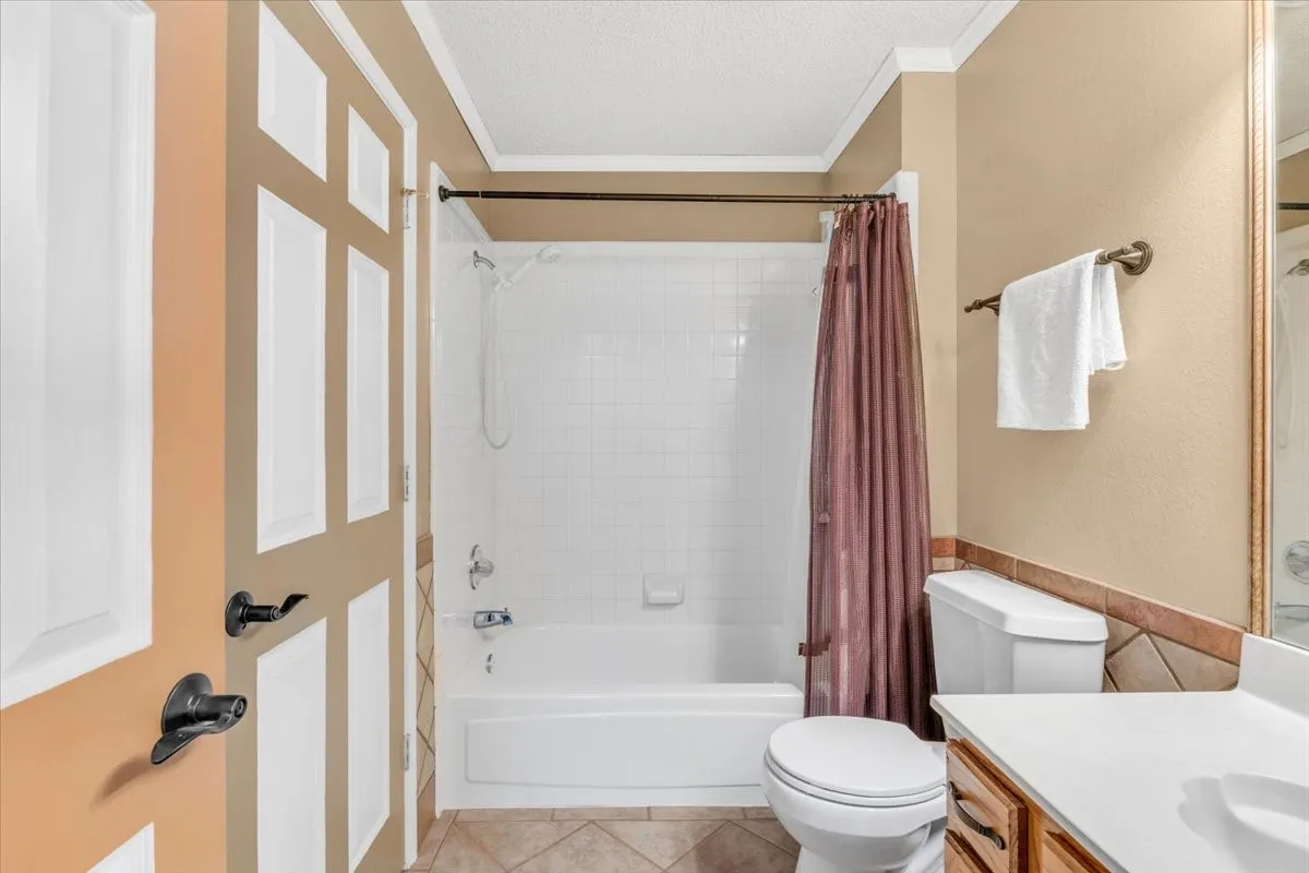 White paneled door with dark hardware, a white tub and shower combination with subway tile surround, tile flooring, and a single vanity with a white countertop.