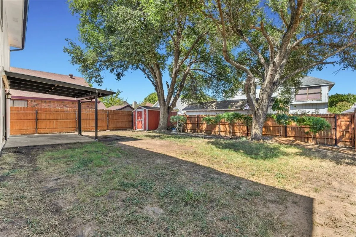 Expansive backyard featuring a covered patio, wood privacy fencing, mature trees, and a Tuff Shed storage shed