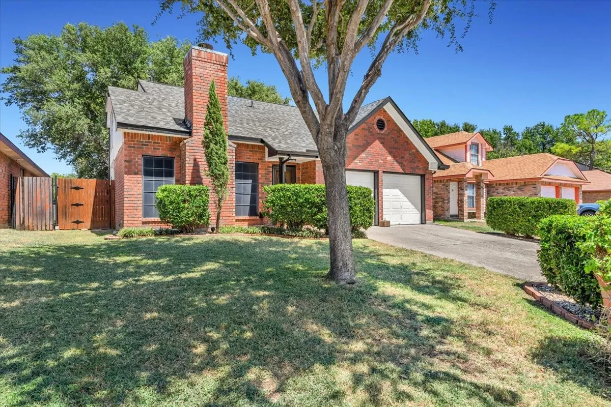 Brick exterior with a prominent chimney, attached two-car garage, and a wood privacy fence