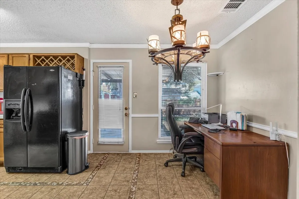 Warm wood cabinetry with integrated wine rack, tile flooring, glass-paned door, crown molding, and decorative chandelier.