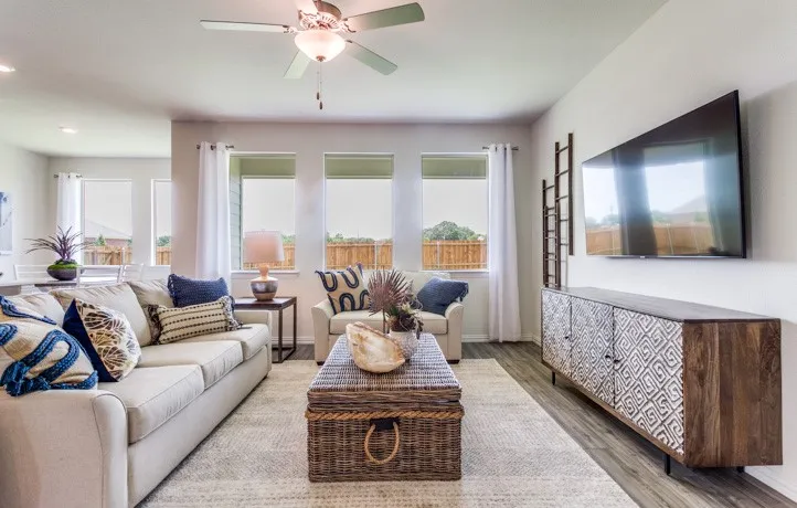 Living area featuring wood-finish flooring, a ceiling fan with integrated lighting, and multiple windows with roller shades