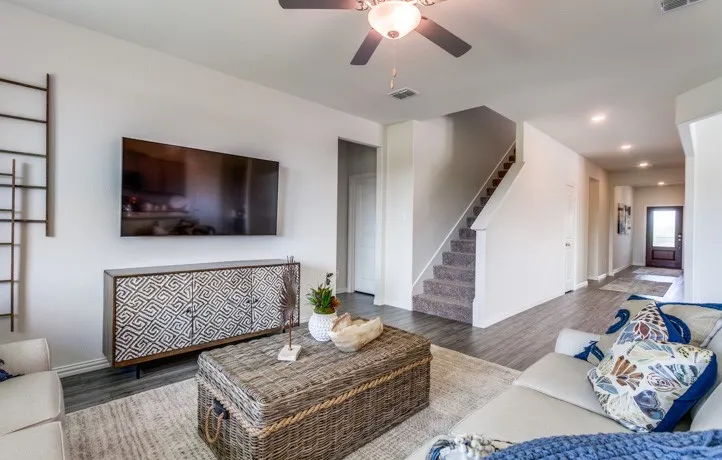 Spacious living area featuring wood-finish flooring, a ceiling fan with integrated lighting, and a staircase with carpeted treads