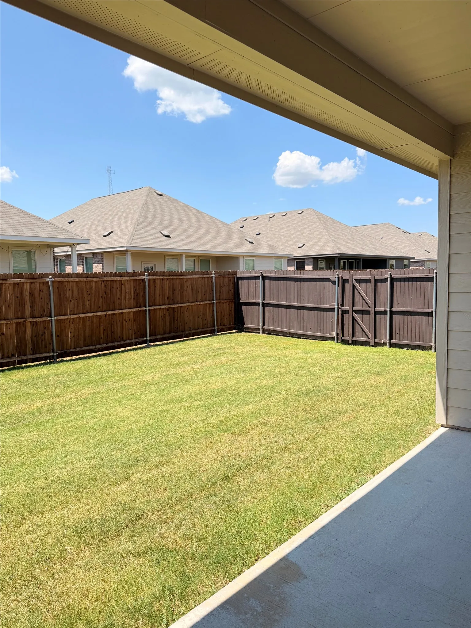 Expansive backyard featuring a lush lawn, privacy fencing, and a concrete patio