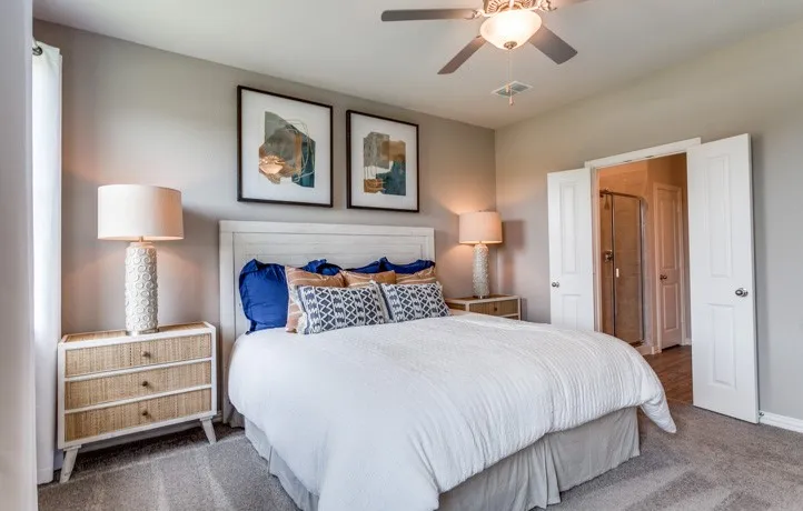 Carpeted bedroom with a built-in ceiling fan, white paneled double doors revealing a shower enclosure, and a white paneled headboard