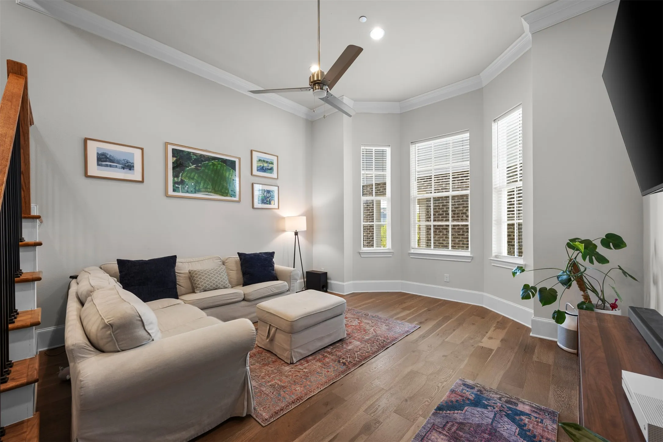 Wood-finish flooring, staircase with wood treads and black railings, bay window with multiple vertical windows, crown molding, and recessed lighting