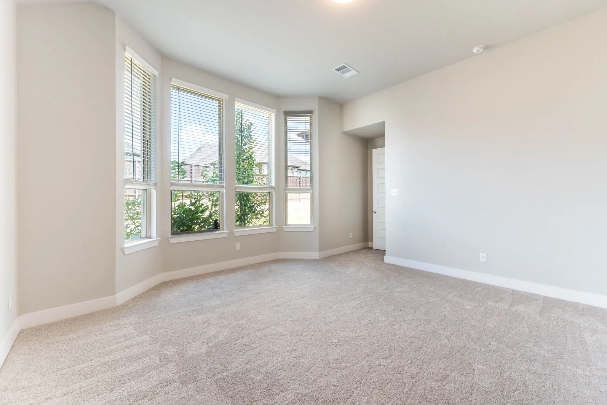 Primary suite Bay window with multiple large windows, neutral carpet flooring, recessed ceiling lighting, and a paneled interior door